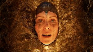A close up of Senua, a Celtic warrior. She wears a leather head dress and has geometric tattoos on her face. She appears to be drowning in a pool of a strange gold liquid.